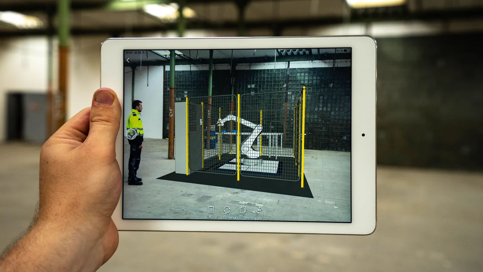 Tablet zeigt eine geplante Roboterzelle per Augmented Reality in einer leeren Halle