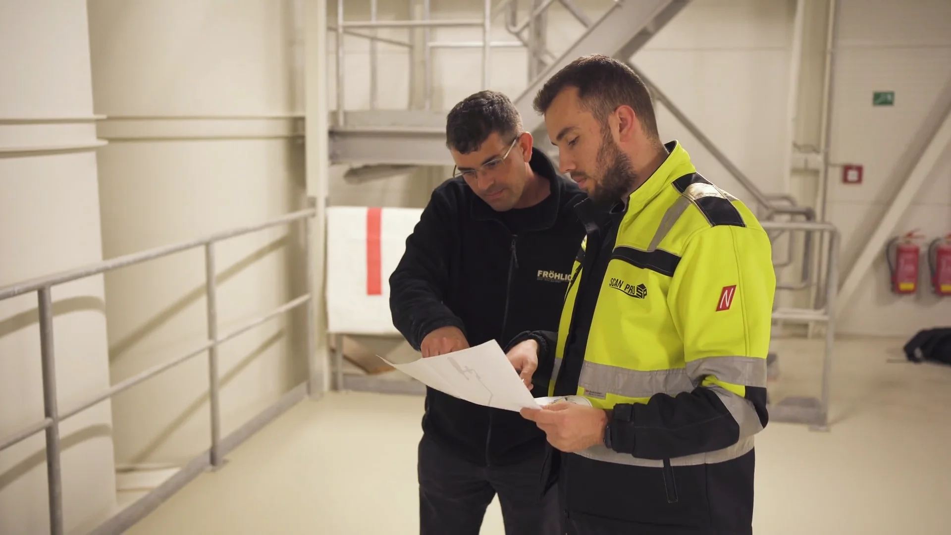 Zwei FRÖHLICH Techniker besprechen einen Anlagenplan vor Ort in der Halle